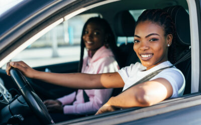 Two beautiful african young cheerful women looking at each other with smile while sitting in car