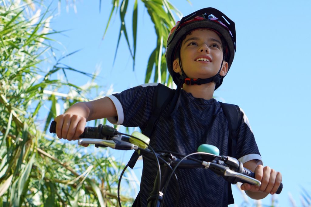preteen boy riding a bike enjoying outdoor sports, with helmet and vegetation in the background