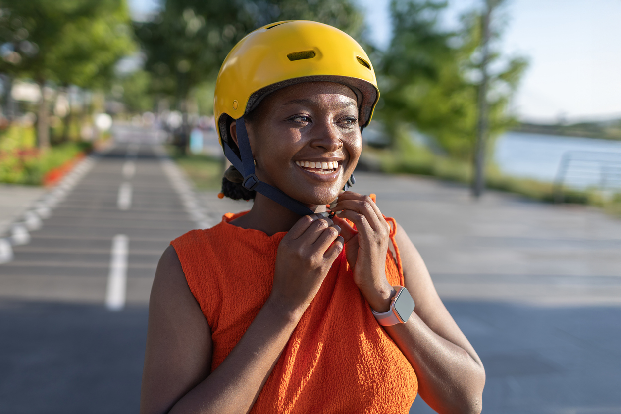 Young African woman prepares to ride bicycle while adjusting yellow helmet